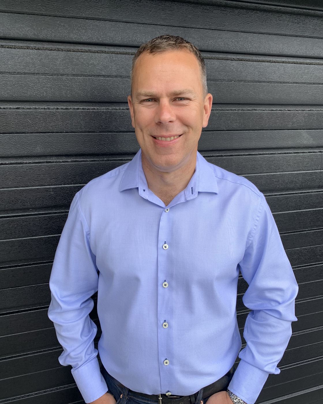 Jon Gordon, who runs Propeller Accounting, standing against a dark corrugated steel wall in a light blue shirt